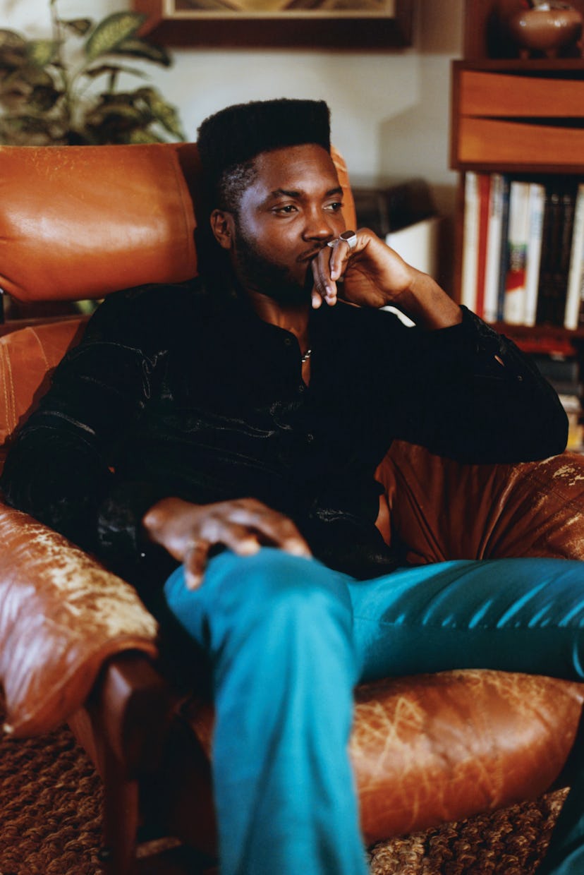 A thoughtful man sits in a leather chair, surrounded by books, with his chin resting on his fist.