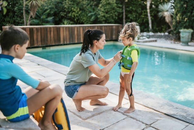 A mom snaps a life jacket on her daughter by the pool.