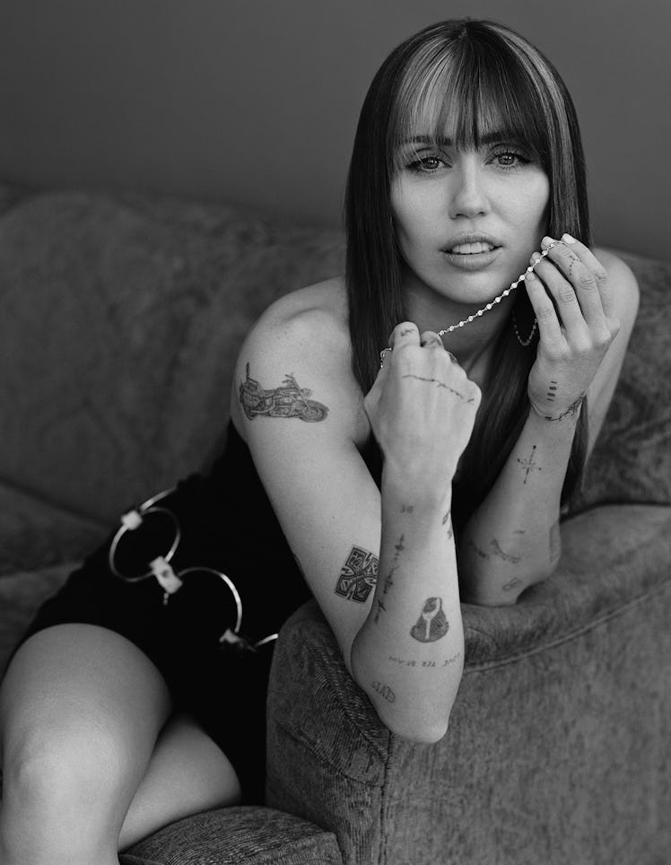 Miley Cyrus wears a black mini dress, vintage loop belt and pearl necklace.