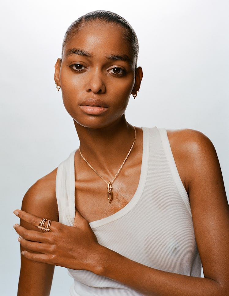 Blésnya wears a white tank top, gold chain and gold rings.
