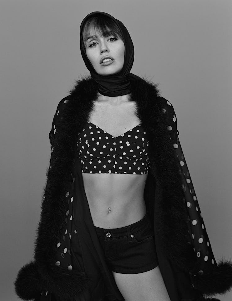 Miley Cyrus wears a black and white polk-a-dot bustier, cape, black headscarf and black denim shorts...