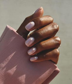 Close-up of a hand with pearl-colored polished nails clutching a pink fabric, highlighted by natural...