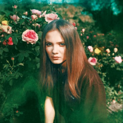 A woman with long hair surrounded by blooming roses, giving a serene look into the camera, captured ...