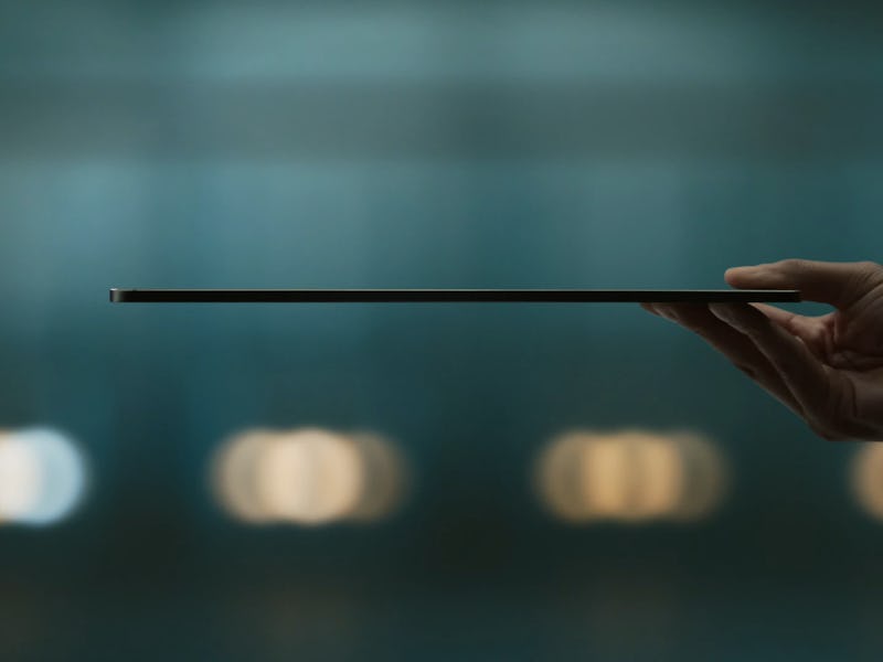 A hand presents the side profile of an ultra-thin laptop against a blurred blue background with soft...
