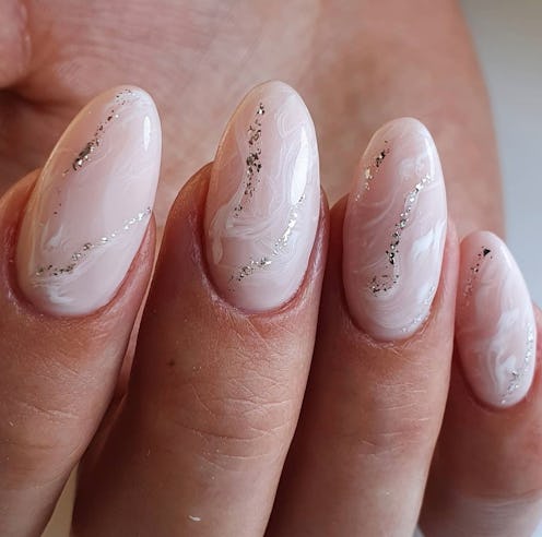 Close-up view of a hand showcasing soft pink marbled manicure with delicate silver glitter accents o...