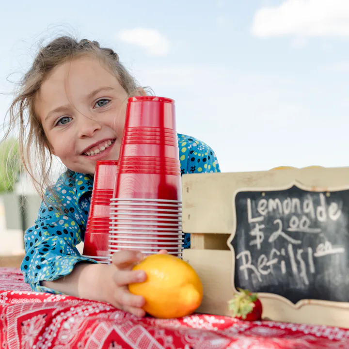 A young girl sells lemonade at her lemonade stand.