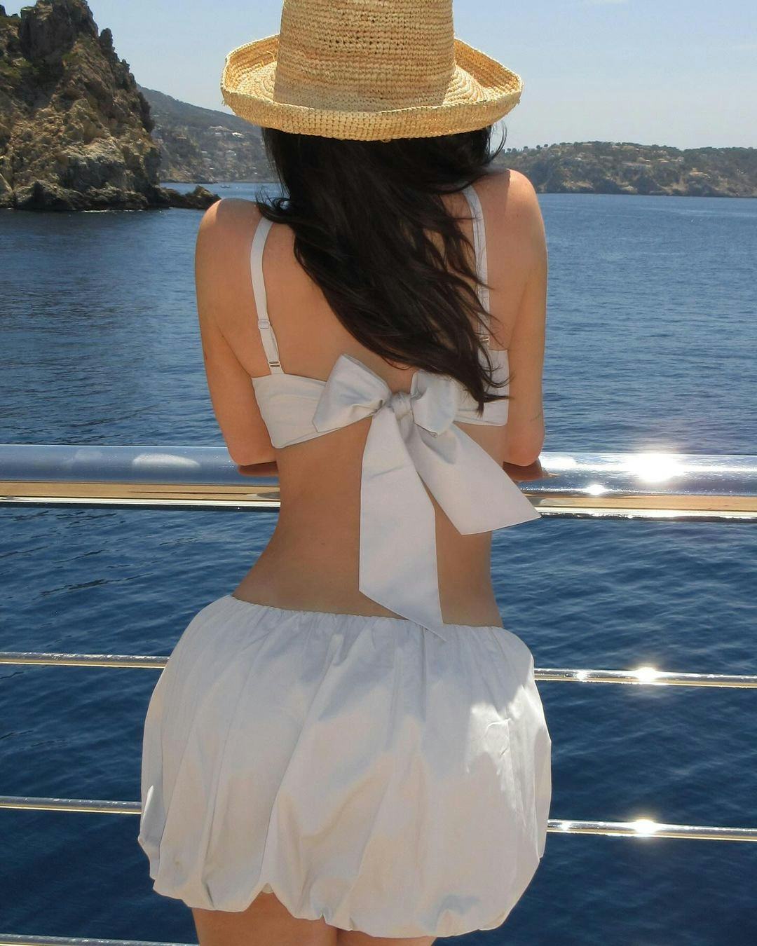 Kylie Jenner wears a white bandeau bra, bubble skirt, and straw hat.