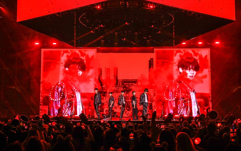 A vibrant concert scene with a band on stage, displayed on a large red-tinted screen, as the audienc...