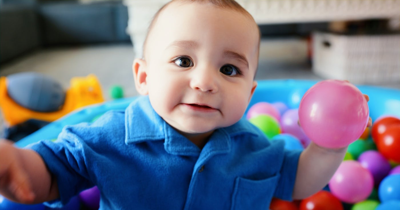 A baby sits in a kiddie pool filled with balls.