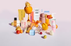 An array of colorful beauty products displayed with vibrant flowers and tropical fruits on a soft pi...