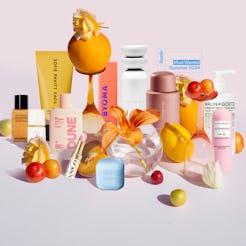 An array of colorful beauty products displayed with vibrant flowers and tropical fruits on a soft pi...