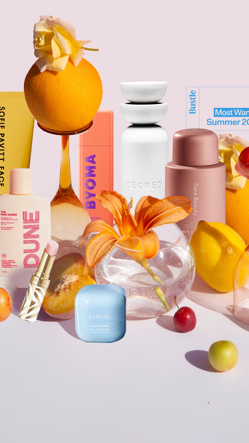 An array of colorful beauty products displayed with vibrant flowers and tropical fruits on a soft pi...