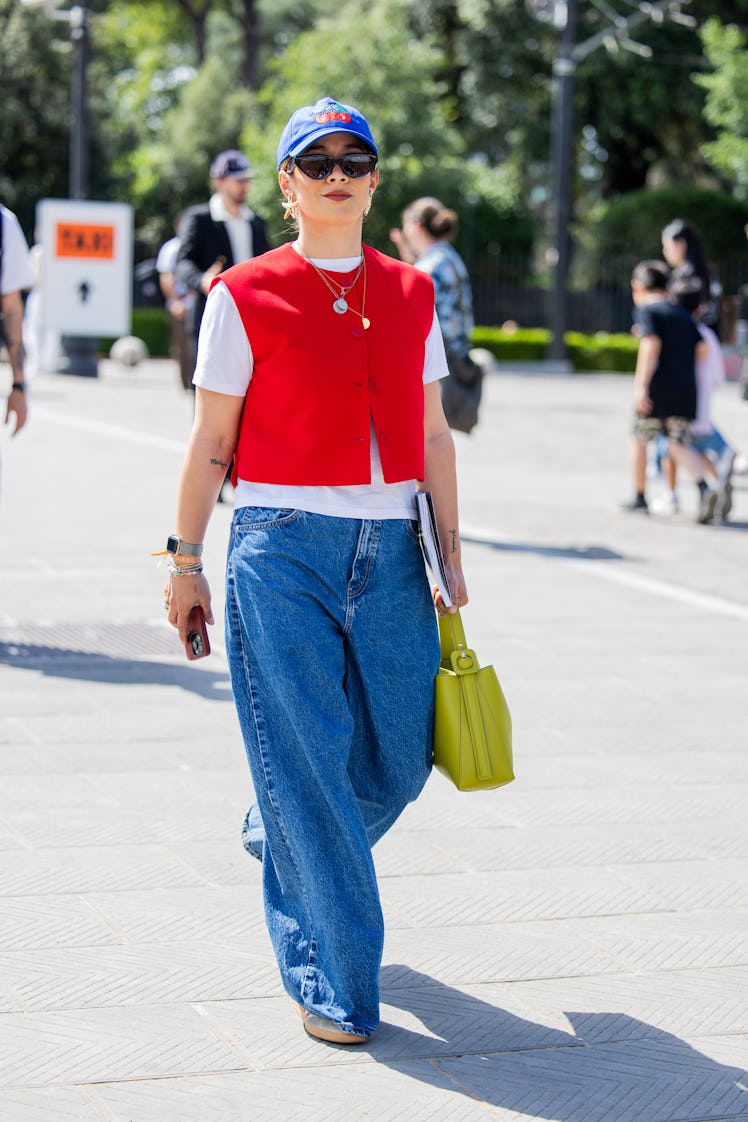 A guest wears red vest, denim jeans, white shirt, cap during Pitti Immagine Uomo 106 on June 12, 202...