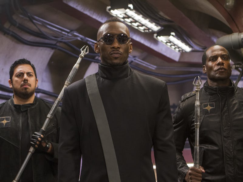 Three men in black combat gear and sunglasses, holding futuristic weapons, stand in a dimly lit indu...