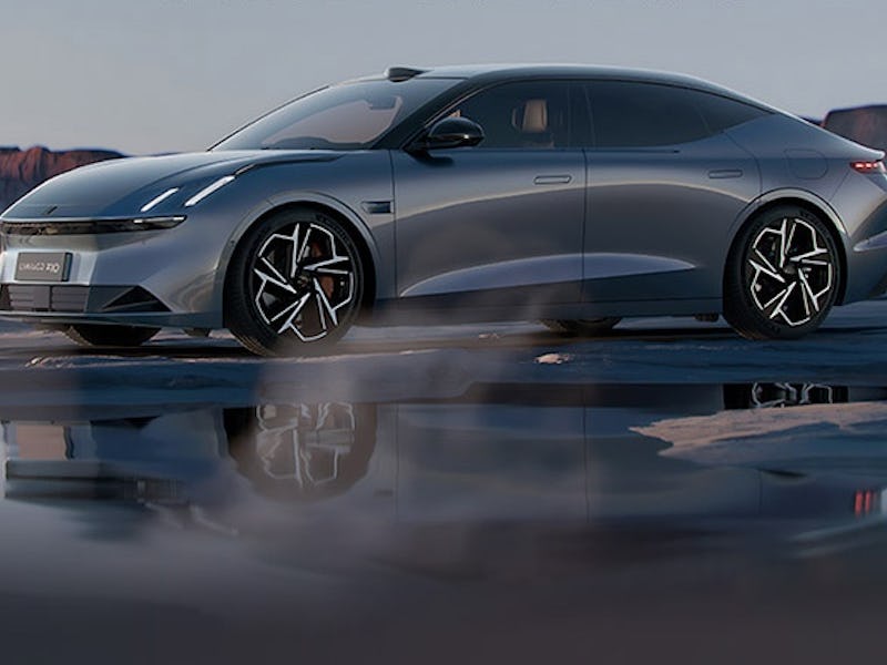 A sleek, silver electric sedan drives on a wet surface, reflecting in the water with a dramatic dese...