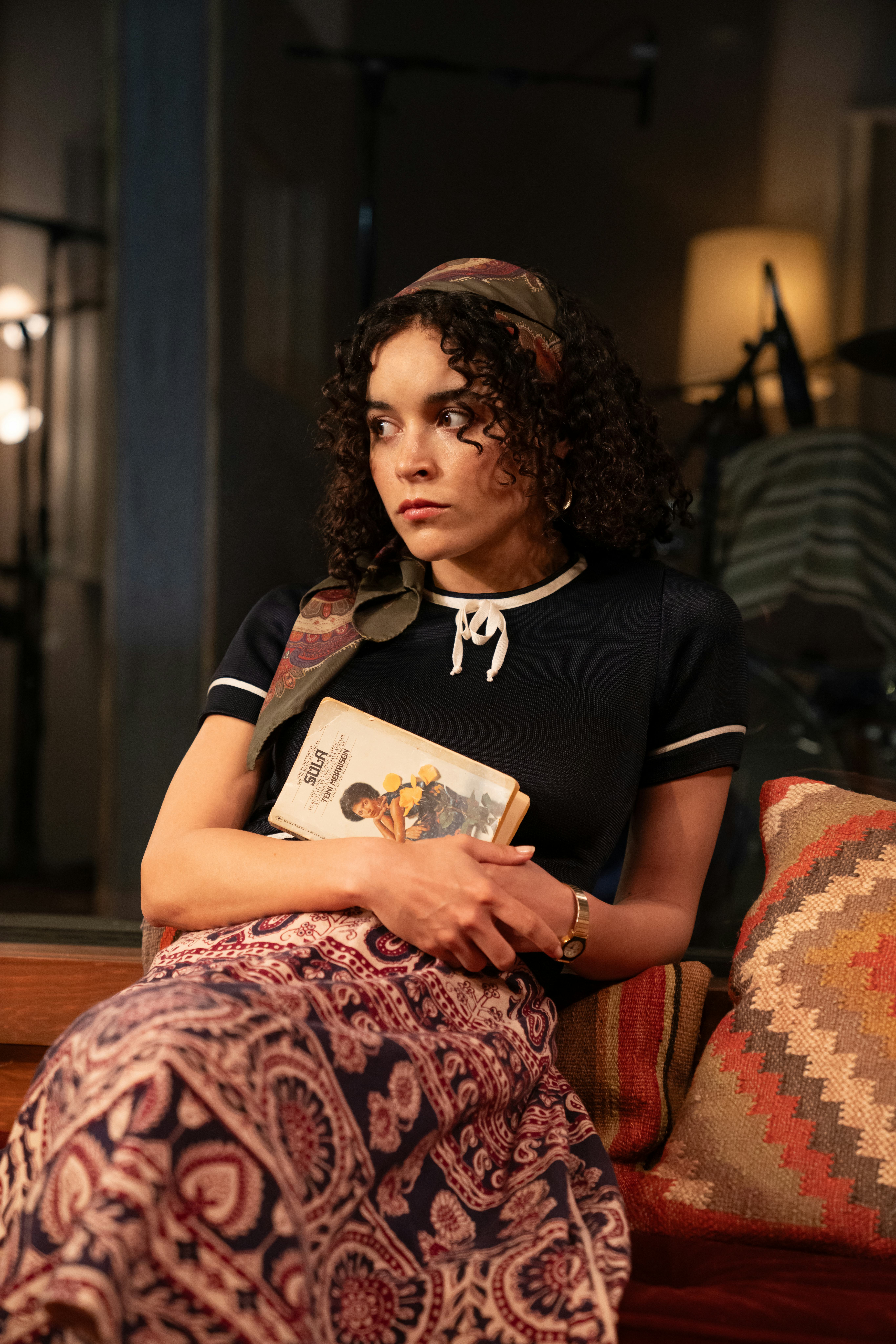 Juliana Canfield sitting on a couch, holding a book, looking away thoughtfully, wearing a casual out&hellip;