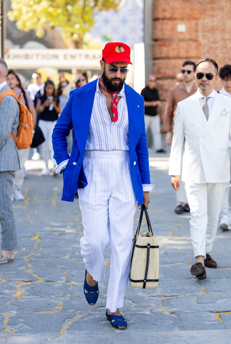A guest wears red cap, blue blazer, white striped pants during Pitti Immagine Uomo 106 on June 11, 2...