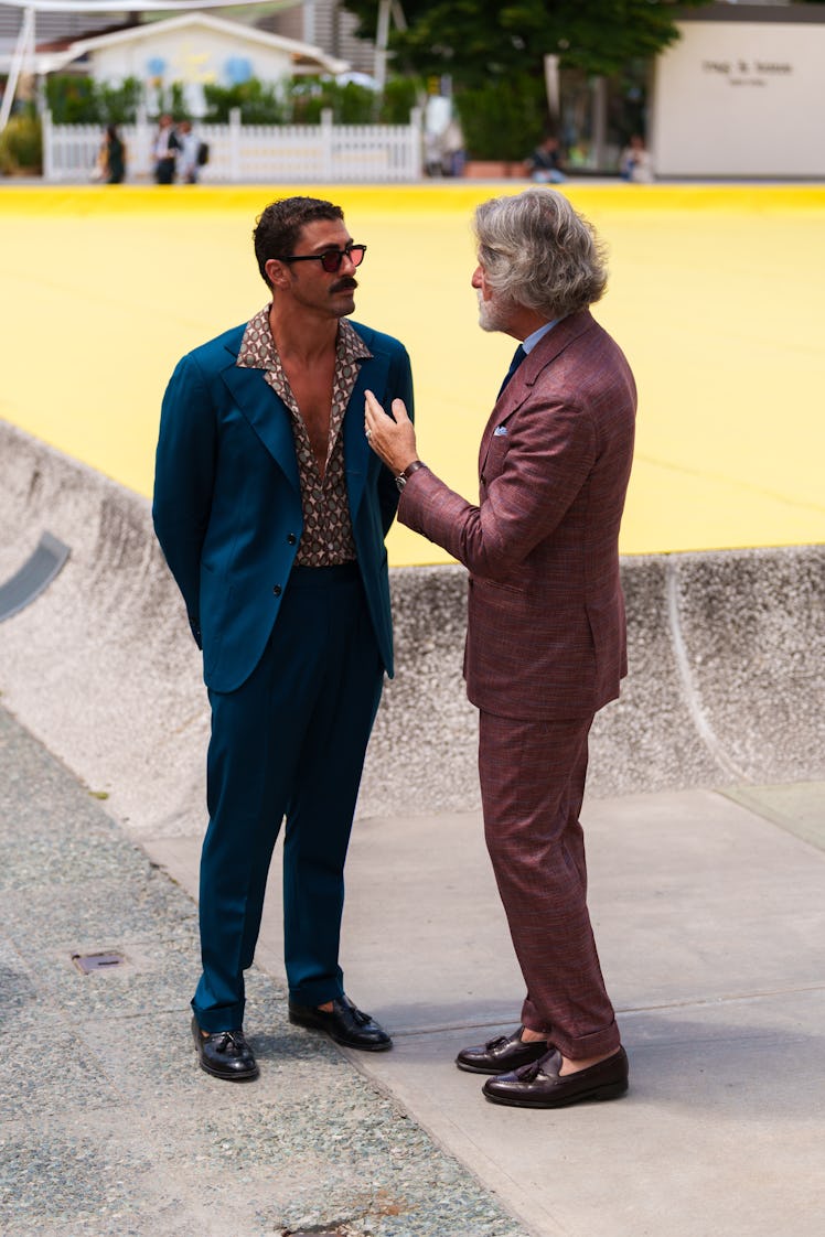 Guests wearing a teal blue suit, dark sunglasses, a burgundy suit are seen during Pitti Immagine Uom...