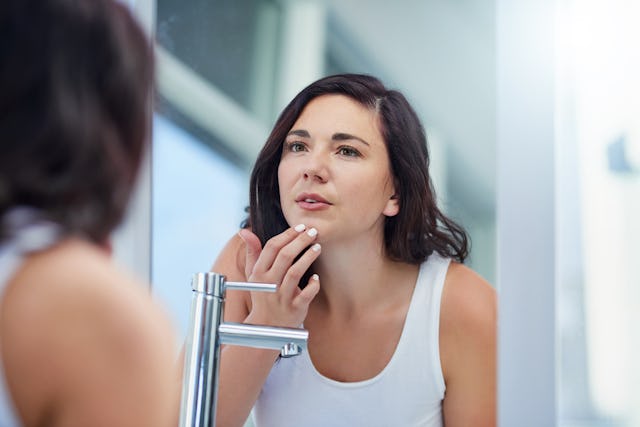 A woman looks at her face in the mirror.