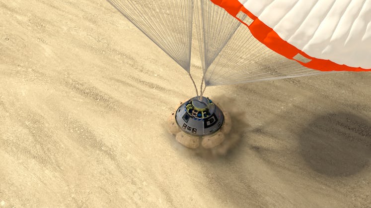 A gumdrop-shaped capsule deploys airbags to cushion its touchdown on a sandy open area. The capsule ...