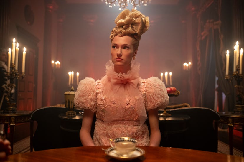 A woman in a period costume sits at a candle-lit table in an ornate, dark room, looking pensive.
