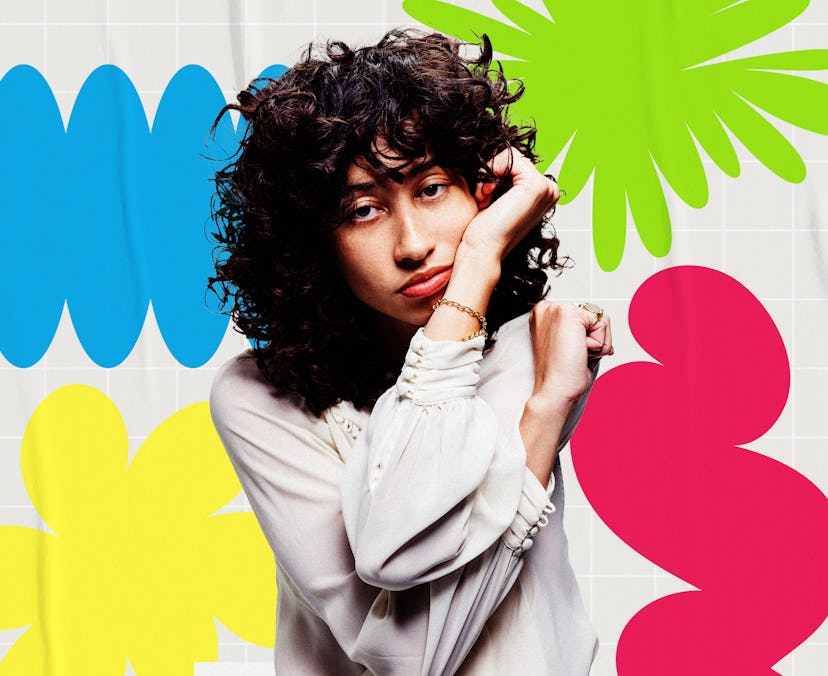 Woman with curly hair posing against a backdrop of colorful flower decals in blue, green, and pink.