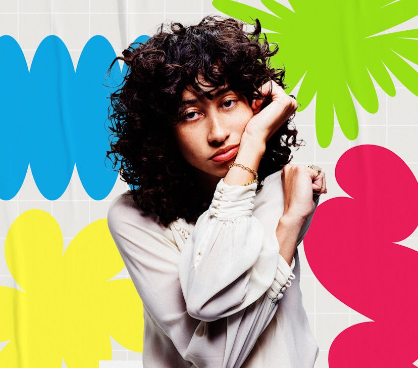 Woman with curly hair posing against a backdrop of colorful flower decals in blue, green, and pink.