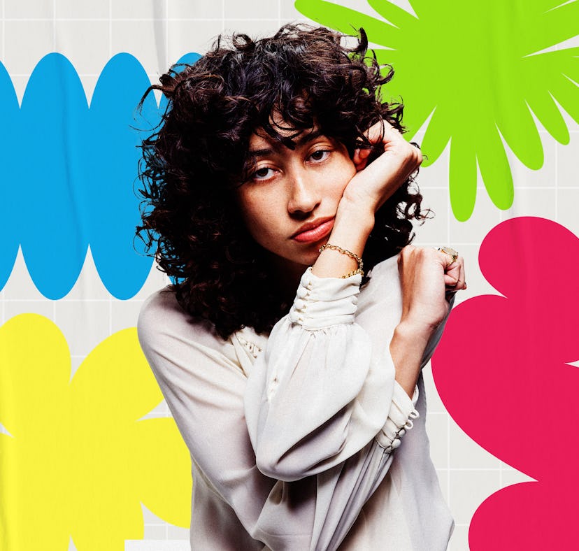 Woman with curly hair posing against a backdrop of colorful flower decals in blue, green, and pink.
