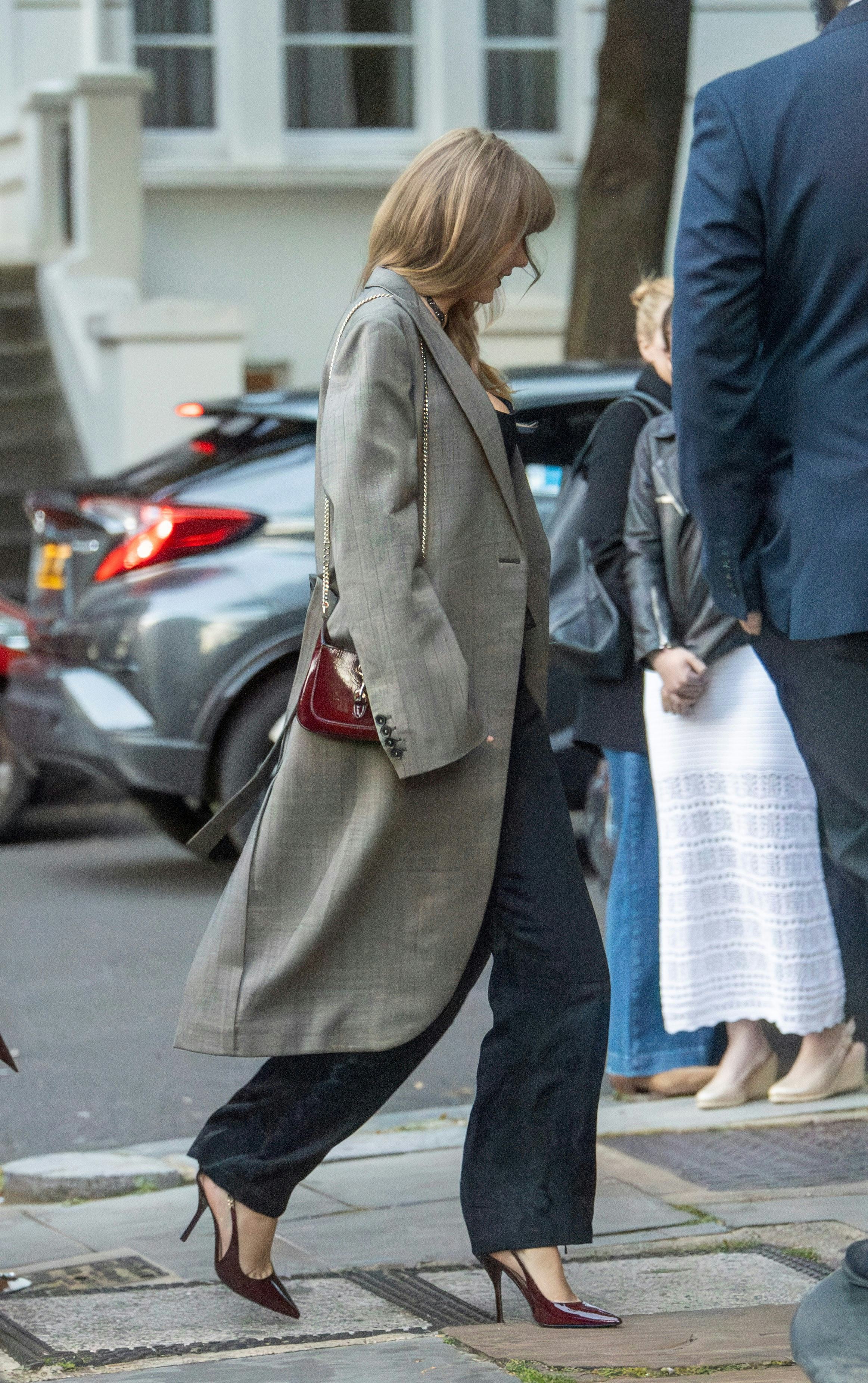 Taylor Swift wears a black corset, pants, gray coat, and red Gucci accessories in London.