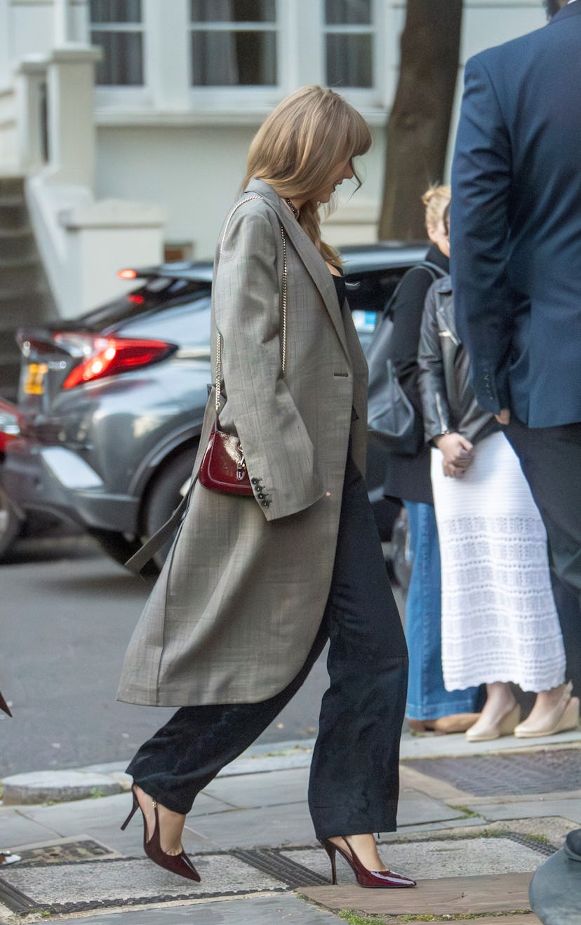 Taylor Swift wears a black corset, pants, gray coat, and red Gucci accessories in London. 