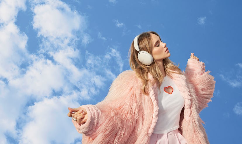 Woman in pink fluffy coat and headphones under blue sky, striking a pose, with a thoughtful expressi...