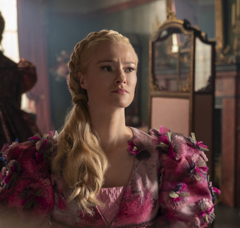 Blonde woman in a pink floral dress sitting in a vintage room, looking pensively to the side, with a...