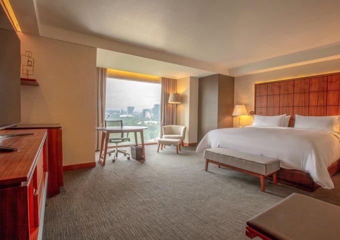 Modern hotel room with a king-sized bed, desk area, and city view from the large window.