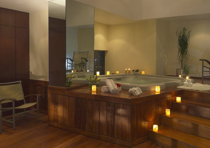 Luxurious spa interior featuring a large hot tub, surrounded by candles, with a cozy seating area nearby.