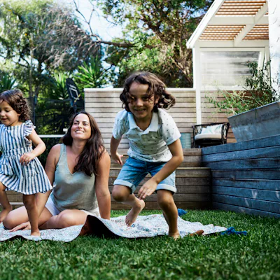 A mom sits on a blanket in the yard as her kids play.