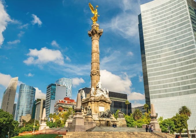 Angel of Independence statue in Mexico City with tall modern buildings and clear blue sky in the background.