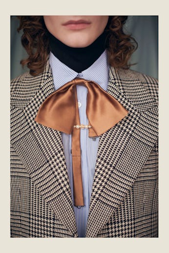Close-up of a stylish outfit featuring a houndstooth blazer, bronze silky bow tie, button-up shirt, ...