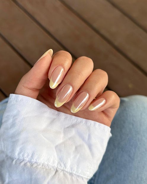 Close-up of a hand showcasing almond-shaped ombre nails, resting on a white shirt sleeve.