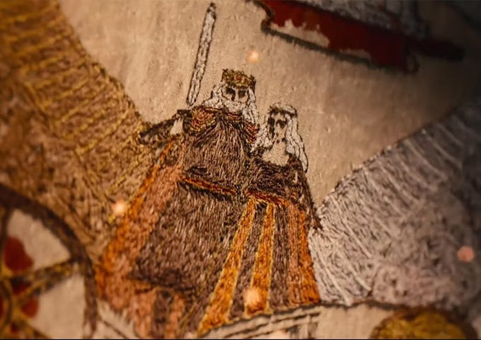 Embroidery depicting a medieval king and queen in ceremonial attire, with a background of intricate designs.