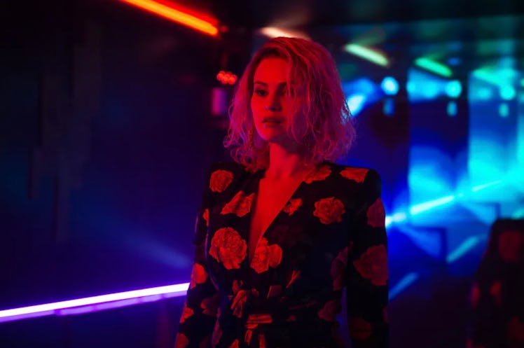 Woman in floral blazer stands in neon-lit corridor, reflecting a vibrant red and blue ambiance.