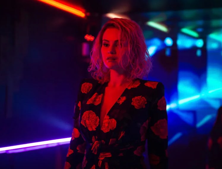 Woman in floral blazer stands in neon-lit corridor, reflecting a vibrant red and blue ambiance.