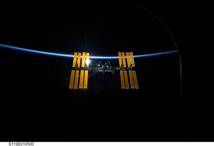 The wings of the International Space Station are backdropped by the blackness of space and the thin ...