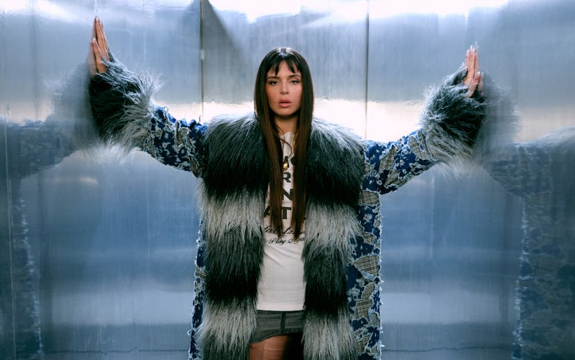 Woman in an elevator wearing a lavish blue and white fur coat, with her arms stretched out touching ...