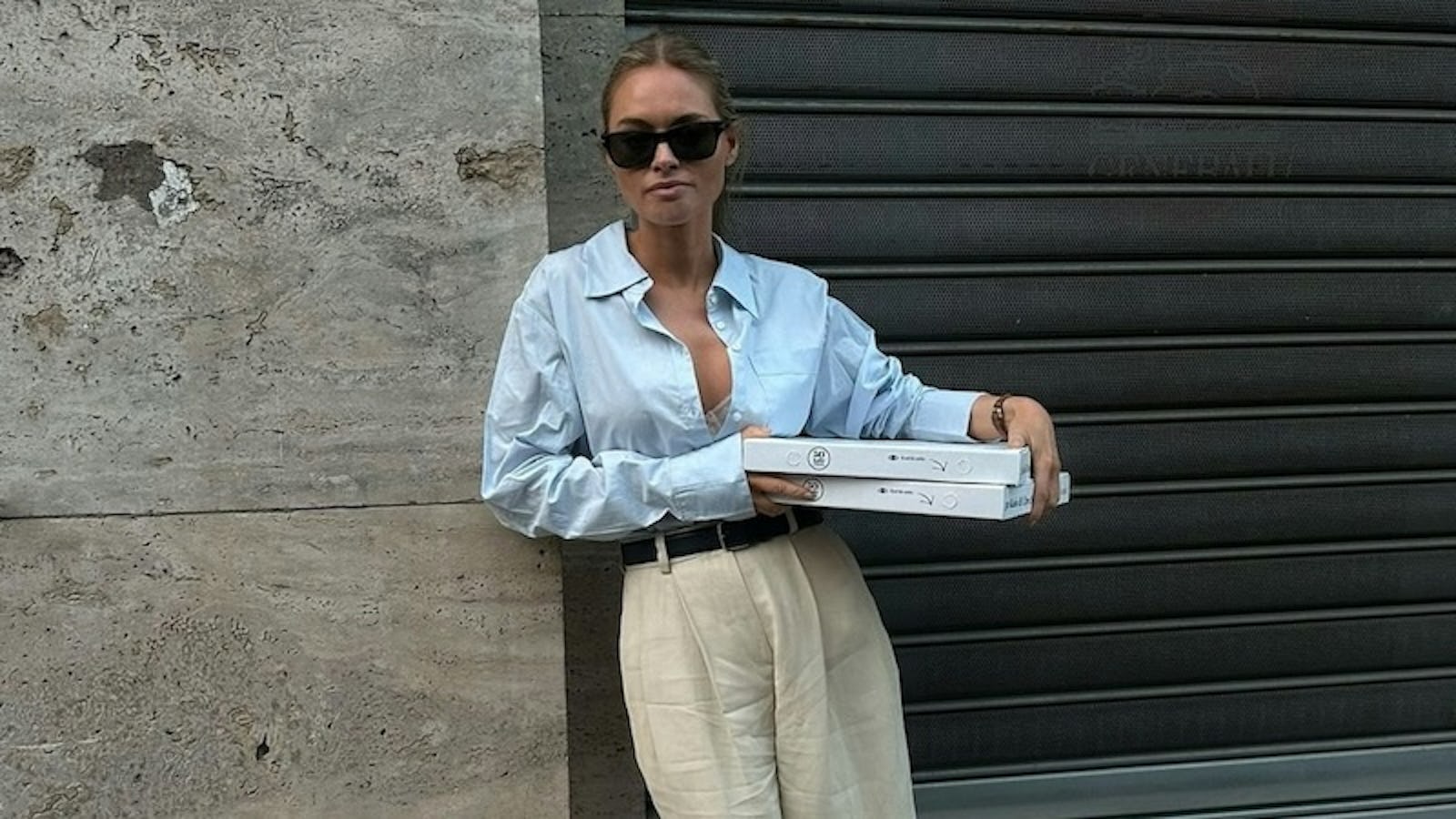 @clairerose wears blue button down and linen shorts holding pizza boxes