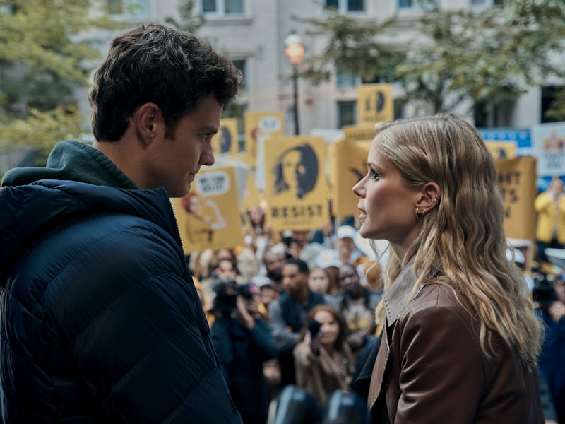 A man and a woman face each other with intense expressions at a crowded protest rally with yellow si...