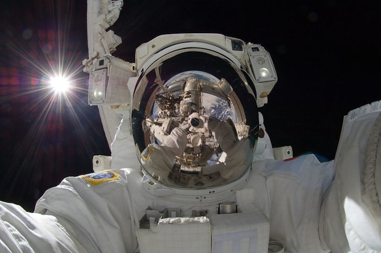 An astronaut in space takes a selfie. The Japanese astronaut wears a spacewalking astronaut suit, an...