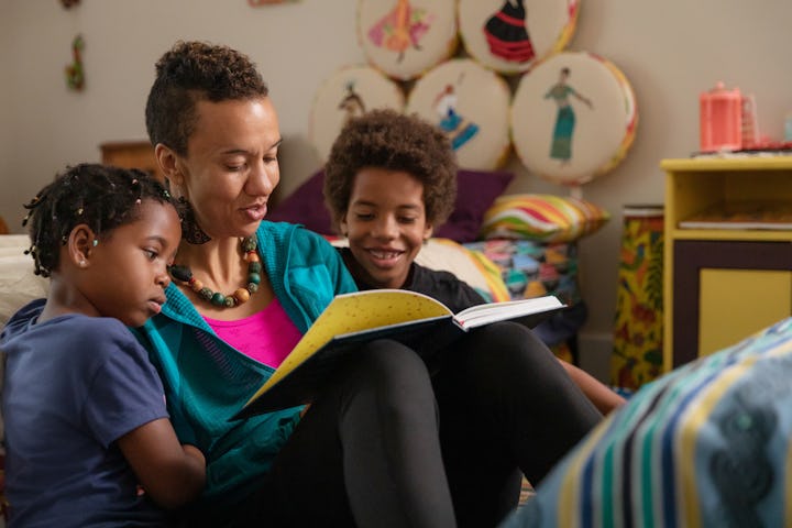 A woman reading a book to two children in a cozy, colorful room decorated with artistic elements.