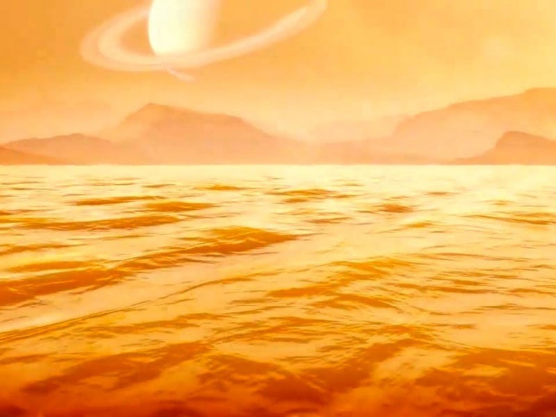 orange-tinted image of a sea, with mountains in the background and a ringed planet in the sky above