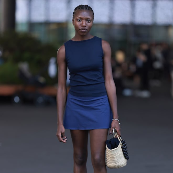 BASEL, SWITZERLAND - JUNE 13: Olamiju Fajemisin is seen wearing a dark blue tank top, a navy blue mini skirt, a silver bracelet, a braided straw bag with black ball chain as pendant and furry clogs with black and white cow pattern on June 13, 2024 in Basel, Switzerland. (Photo by Jeremy Moeller/Getty Images)