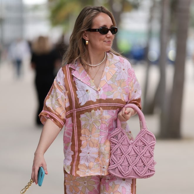 MIAMI, FLORIDA - DECEMBER 08: Anna Sophie seen wearing Le Specs brown oval sunglasses, gold earrings and necklace, pearl necklace, pink colorful floral print pattern shirt / blouse, matching pink colorful floral print pattern long pants, pink crochet handbag , on December 08, 2023 in Miami, Florida. (Photo by Jeremy Moeller/Getty Images)